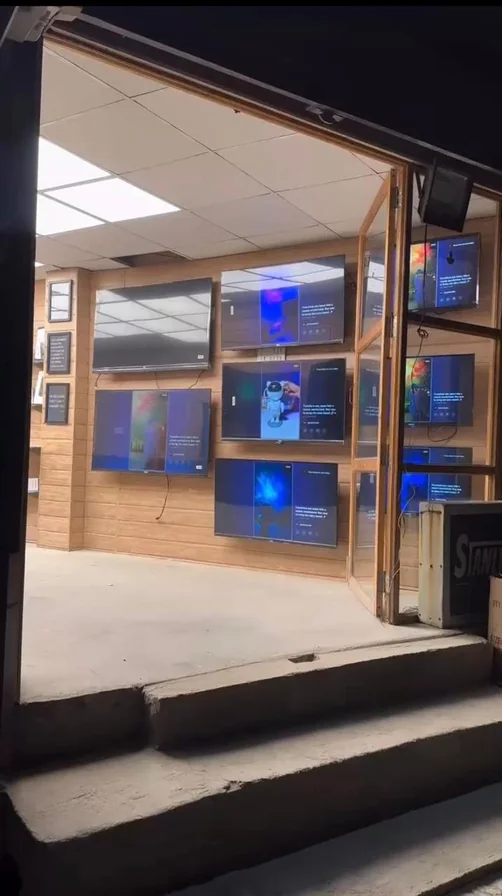 A Stanlee storefront at night, the wall of lit panels visible from the street